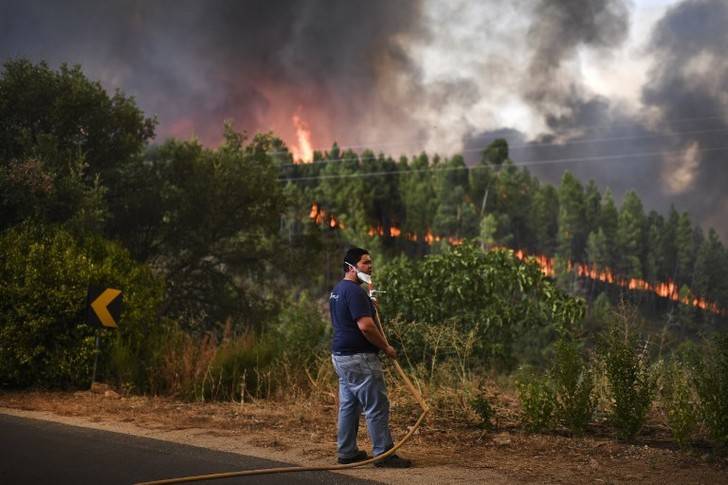   Un villageois tient un tuyau d’arrosage alors que l’incendie se rapproche de sa maison, le 25 juillet 2017 à Macao, au Portugal. / PATRICIA DE MELO MOREIRA / AFP